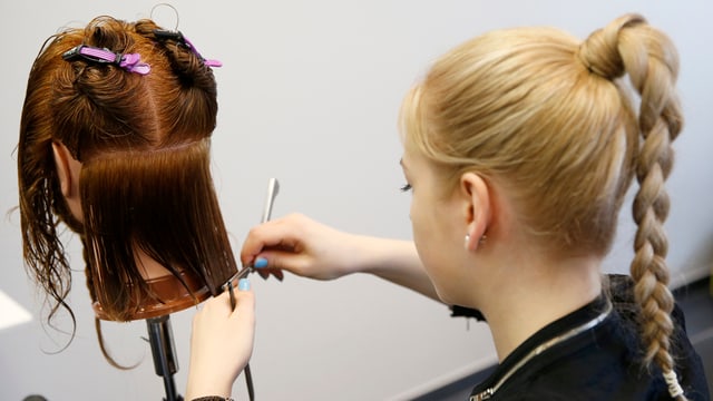 Coiffeur-Lehrling schneidet Haare an einer Perücke