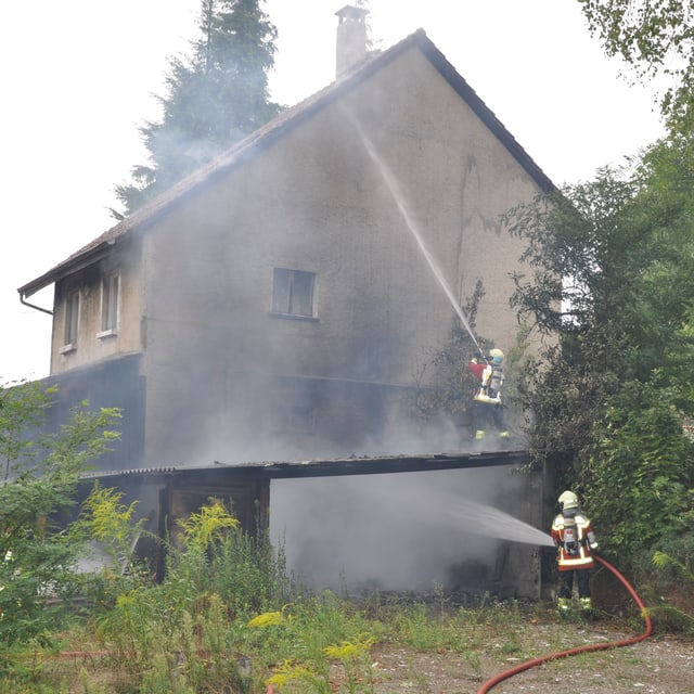 Zwei Feuerwehrleute spritzen Wasser an eine Hausfassade Zwei Feuerwehrleute spritzen Wasser an eine Hausfassade
