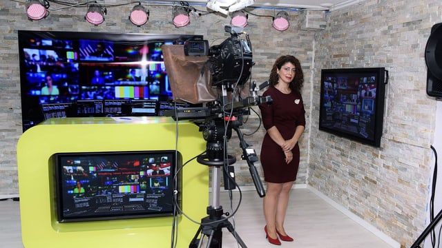 Eine Frau steht in einem Fernsehstudio. Im Vordergrund ist eine Kamera zu sehen. Eine Frau steht in einem Fernsehstudio. Im Vordergrund ist eine Kamera zu sehen.