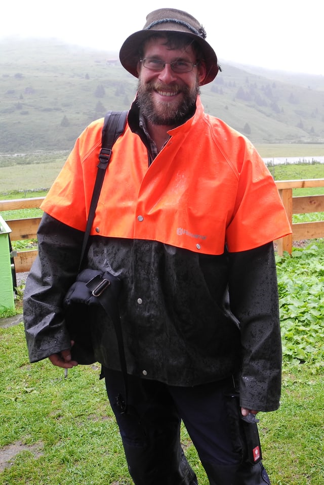 Ludwig Willmann mit orangefarbenem, regendichtem Umhang über wetterfester Kleidung und seiner Tasche mit wichtigen Utensilien über der Schulter. Ludwig Willmann mit orangefarbenem, regendichtem Umhang über wetterfester Kleidung und seiner Tasche mit wichtigen Utensilien über der Schulter.