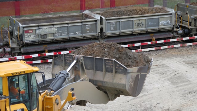 Ein Pneulader mit Dreck in der Schaufel, im Hintergrund Bahnwagen Ein Pneulader mit Dreck in der Schaufel, im Hintergrund Bahnwagen