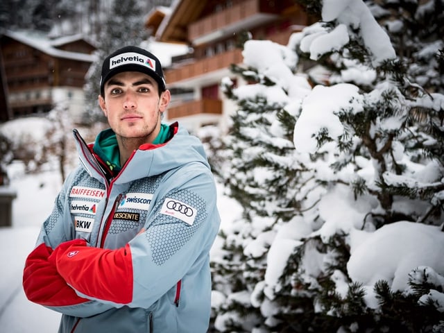Daniel Yule steht mit verschränkten Armen vor einer verschneiten Tanne.
