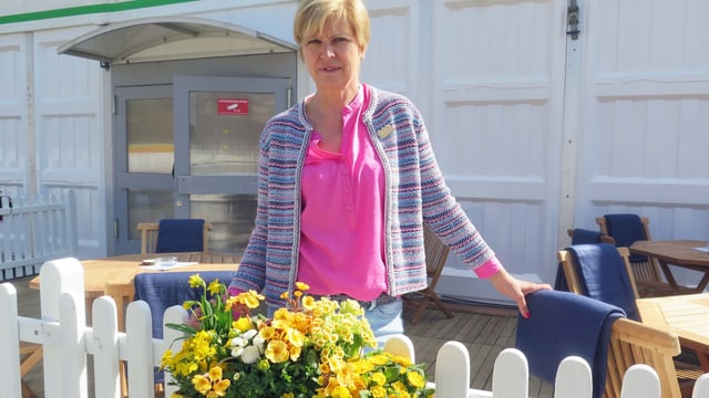 Frau steht hinter Zaun mit Blumenschmuck Frau steht hinter Zaun mit Blumenschmuck