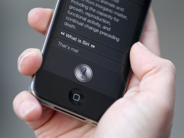 Hand hält iPhone, auf dem Bildschirm ist Siri aufgerufen Hand hält iPhone, auf dem Bildschirm ist Siri aufgerufen