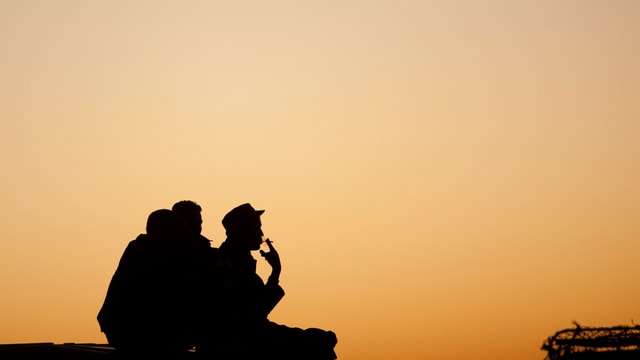 Soldaten sitzen rauchend vor einem gelben Himmel. 