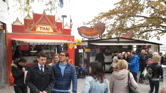 Leute an einem Jahrmarkt vor einem Essstand der Thai-Küche anbietet. Leute an einem Jahrmarkt vor einem Essstand der Thai-Küche anbietet.