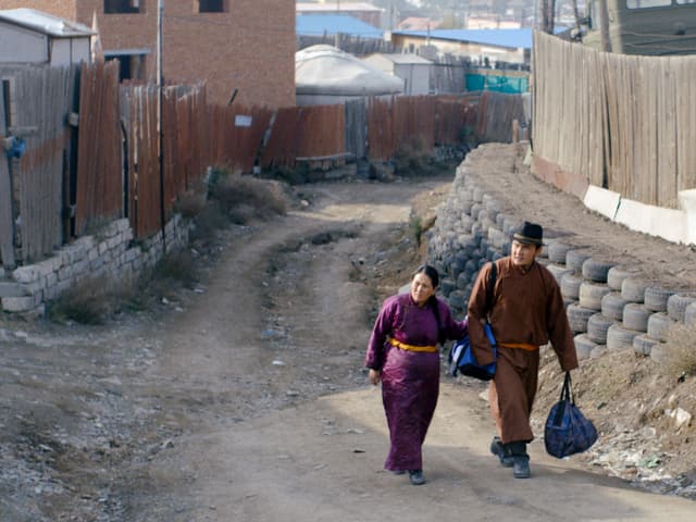 Zwei Personen in traditionellen mongolischen Kleidern gehen durch eine Stadt. Zwei Personen in traditionellen mongolischen Kleidern gehen durch eine Stadt.