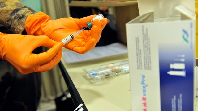 Behandschuhte Hände ziehen eine Spritze mit dem Impfstoff auf.