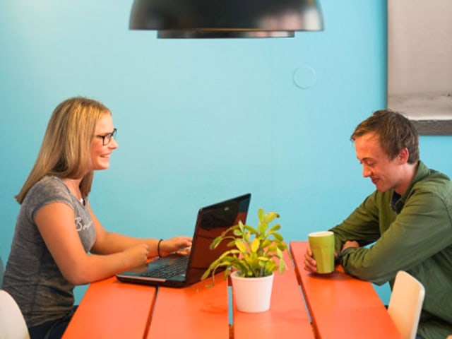 Eine Frau und ein Mann sitzen an einem orangen Tisch. Sie bedient einen Laptop. Eine Frau und ein Mann sitzen an einem orangen Tisch. Sie bedient einen Laptop.