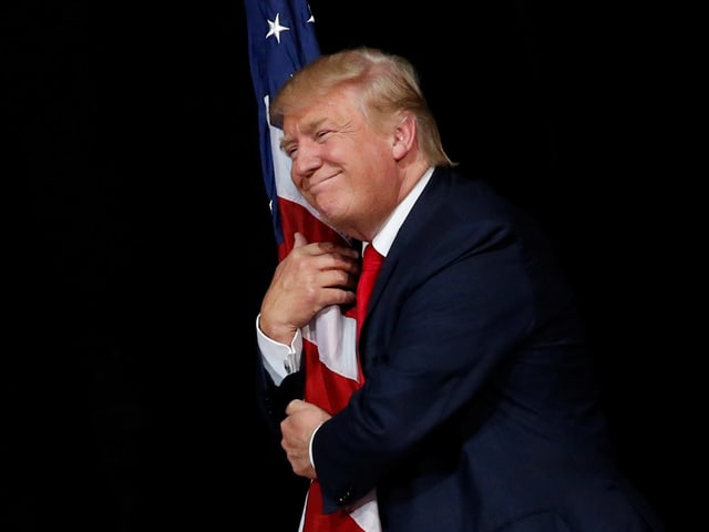 Trump umarmt eine US-Flagge. Trump umarmt eine US-Flagge.