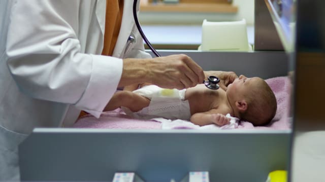 Ein Arzt setzt sein Stetoskop auf die Brust eines Babys.