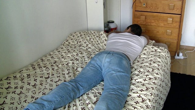 "Carlos" liegt auf dem Bauch auf einem Bett, die Arme verschränkt unter dem Kopf