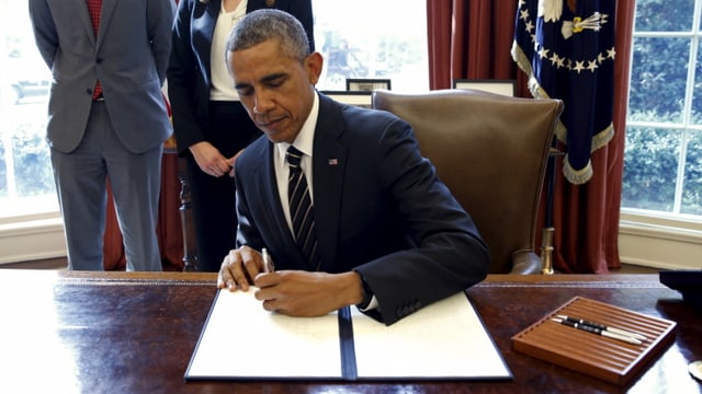 Barack Obama unterzeichnet an einem Schreibtisch ein Dekret. Barack Obama unterzeichnet an einem Schreibtisch ein Dekret.