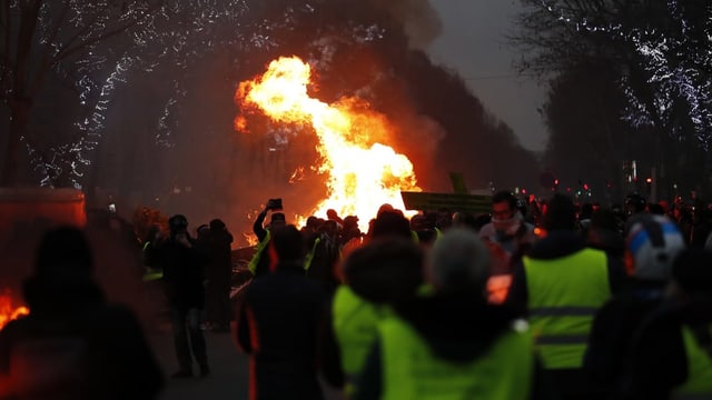 Demonstranten, im Hintergrund steigt Rauch und Feuer auf. Demonstranten, im Hintergrund steigt Rauch und Feuer auf.