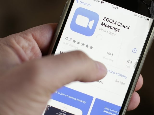 Hand hält Handy mit Zoom-Logo auf dem Display. Hand hält Handy mit Zoom-Logo auf dem Display.