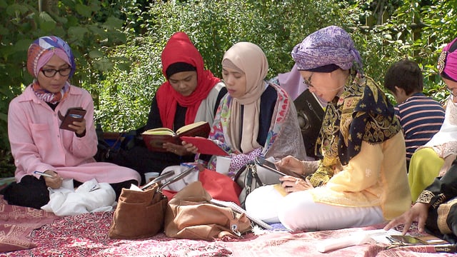 Muslimische Frauen sitzen in einem Garten auf bunten Tüchern Muslimische Frauen sitzen in einem Garten auf bunten Tüchern