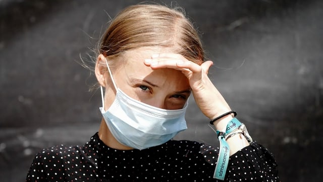Greta Thunberg trägt eine Hygienemaske und blickt ernst in die Kamera, eine Hand an der Stirn, um die Augen von der Sonne abzuschirmen. Greta Thunberg trägt eine Hygienemaske und blickt ernst in die Kamera, eine Hand an der Stirn, um die Augen von der Sonne abzuschirmen.