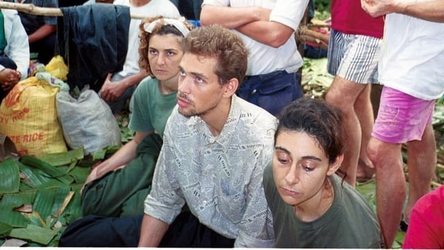 Zwei junge Frauen und ein junger Mann sitzen auf dem Boden, um sie herum andere Menschen. Zwei junge Frauen und ein junger Mann sitzen auf dem Boden, um sie herum andere Menschen.