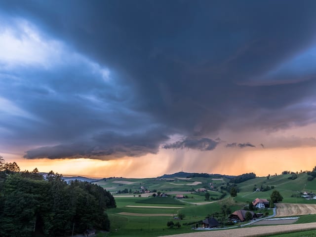 Landschaft in der Abendsonne mit dunklen Wolken am Himmel. Am Horizont fallen Regenstreifen.