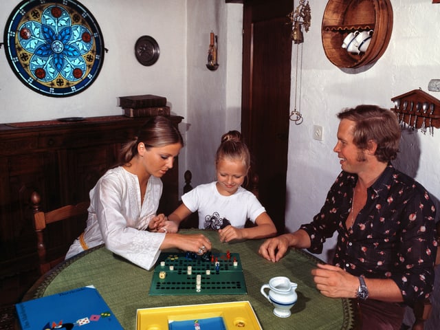 Die junge Familie spielt Halma im rustikal eingerichteten Wohnzimmer. Die junge Familie spielt Halma im rustikal eingerichteten Wohnzimmer.