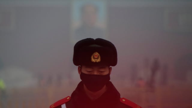 Chinesischer Beamte mit Maske vor Mao-Plakat im Dunst Chinesischer Beamte mit Maske vor Mao-Plakat im Dunst