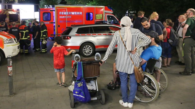 Leute stehen herum. Ein Feuerwehrwagen. Leute stehen herum. Ein Feuerwehrwagen.