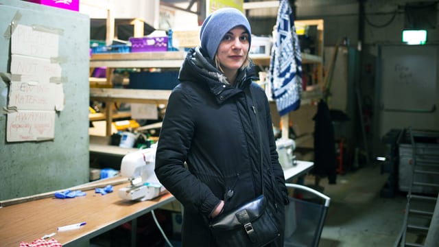 Eine junge Frau steht warm eingepackt in einer Lagerhalle. Eine junge Frau steht warm eingepackt in einer Lagerhalle.