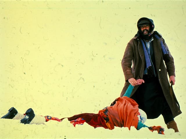 Filmstill: Ein Mann hebt den Arm eines leblos am Boden liegenden Menschen. Filmstill: Ein Mann hebt den Arm eines leblos am Boden liegenden Menschen.