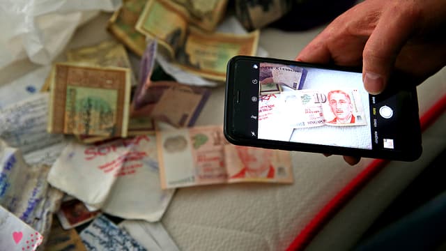 Eine Männerhand mit einem Handy. Er macht eine Aufnahme von einem Bett mit Geld darauf. Eine Männerhand mit einem Handy. Er macht eine Aufnahme von einem Bett mit Geld darauf.