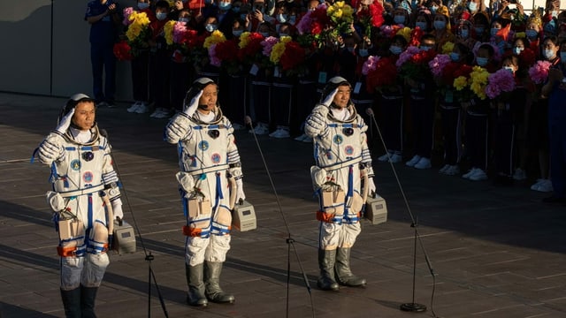 Drei Astronauten salutieren neben einer Menschenmenge. Drei Astronauten salutieren neben einer Menschenmenge.