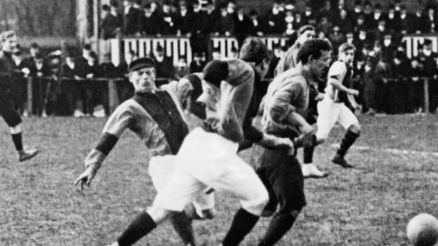 Ein Fussballspiel von früher, die Fussballer in langen Hosen und mit Mützen Ein Fussballspiel von früher, die Fussballer in langen Hosen und mit Mützen
