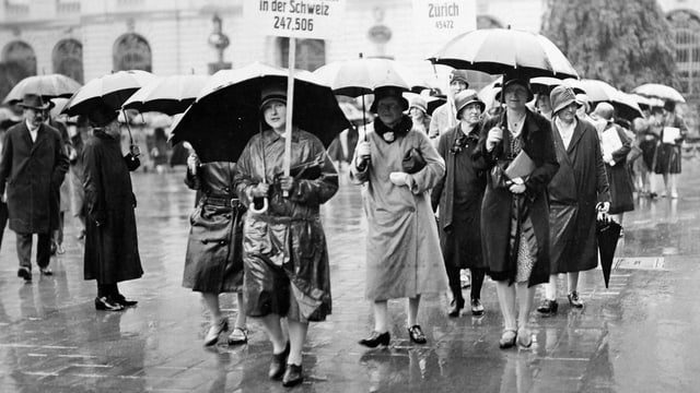 Eine Gruppe von Frauen protestiert im Regen für das Frauenstimmrecht. Eine Gruppe von Frauen protestiert im Regen für das Frauenstimmrecht.