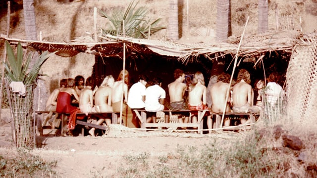 Eine Gruppe junger, nackter Leute sitzt in einer Strohhütte einer Strandbar. Eine Gruppe junger, nackter Leute sitzt in einer Strohhütte einer Strandbar.
