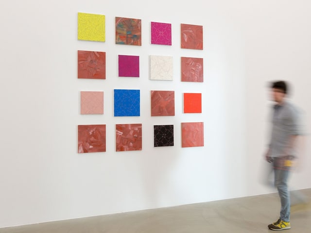 Quadratische Bilder auf einer weissen Wand im Museum. Davor läuft ein junger Mann vorbei. Quadratische Bilder auf einer weissen Wand im Museum. Davor läuft ein junger Mann vorbei.