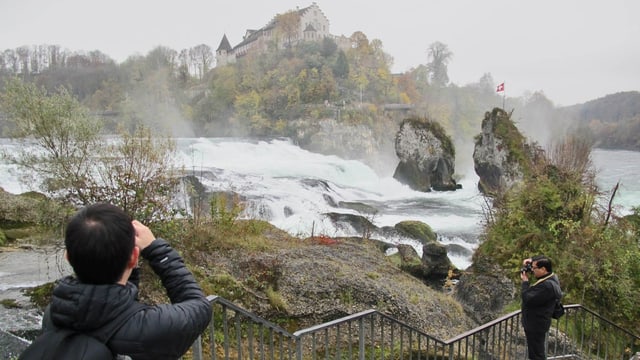 Zwei Touristen in schwarzen Jacken fotografieren den Rheinfall.