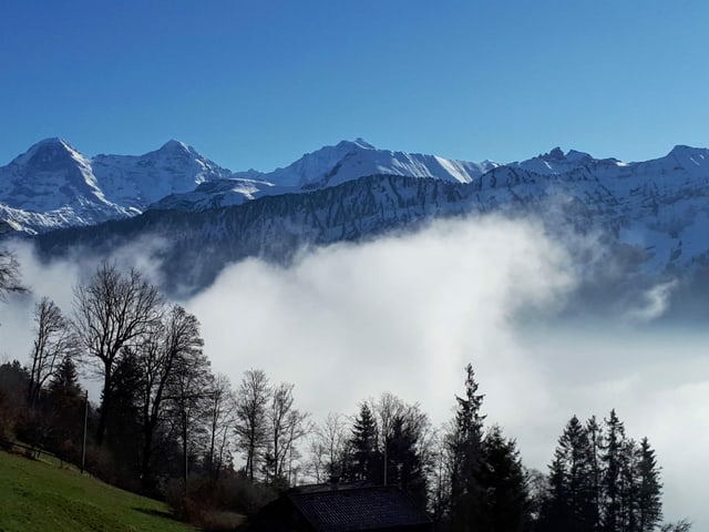 Nebelfetzen in den Bergen, darüber strahlend blauer Himmel.