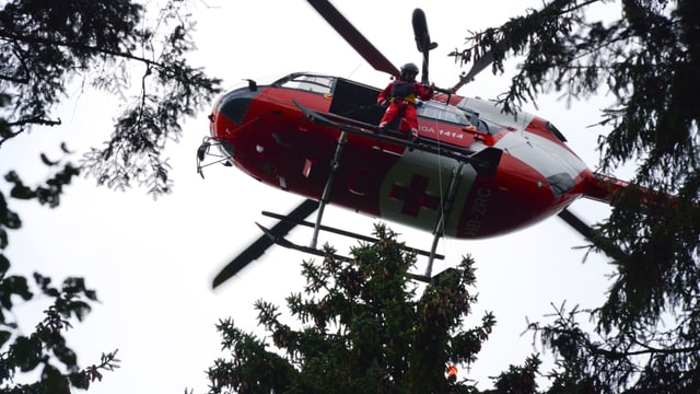 Hubschrauber mit offener Tür, Rettungssanitäter lässt Winde herunter Hubschrauber mit offener Tür, Rettungssanitäter lässt Winde herunter