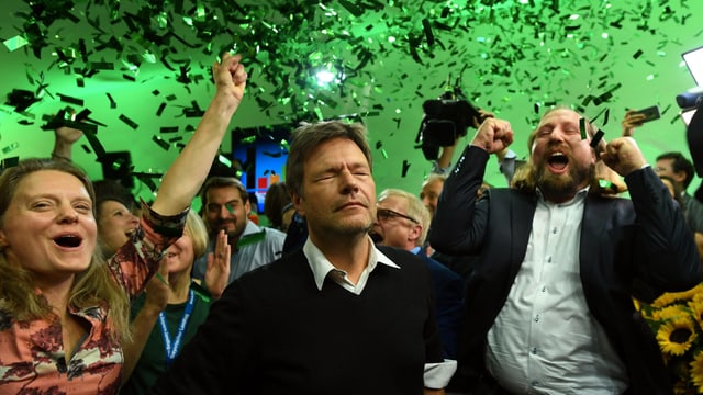 Habeck steht mit geschlossenen Augen neben jubelnden Parteikollegen, von der Decke regnen in grünem Licht grüne Glitzerschnipsel. Habeck steht mit geschlossenen Augen neben jubelnden Parteikollegen, von der Decke regnen in grünem Licht grüne Glitzerschnipsel.
