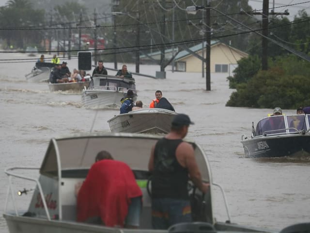 People drive motor boats on the flooded road.