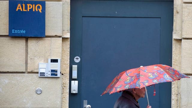 Ein Mann mit Regenschirm läuft an einem Hauseingang eines Alpiq-Gebäudes vorbei. Ein Mann mit Regenschirm läuft an einem Hauseingang eines Alpiq-Gebäudes vorbei.