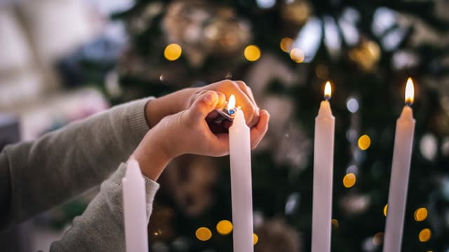 Eine Kinderhand zündet Kerzen an, im Hintergrund ein Weihnachtsbaum.