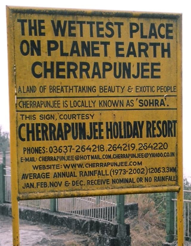 Gelbe Strassentafel mit dem Text "THE WETTEST PLACE ON PLANET EARTH CHERRAPUNJEE"