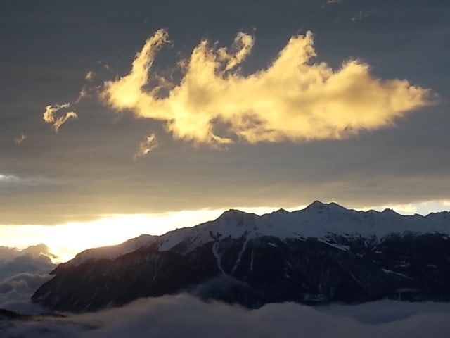 Berglandschaft. Im Tal Nebel, am Himmel im Hintergrund dunkle Wolken und im Vordergrund eine helle, gelbe Wolke.