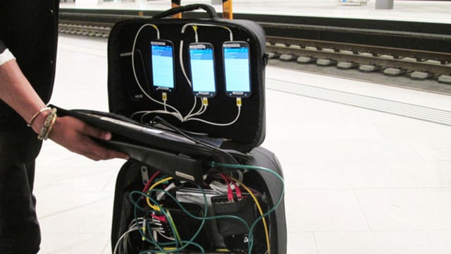 In einem Koffer stecken drei Handys, die mit Kabeln mit Messtechnik verbunden sind. In einem Koffer stecken drei Handys, die mit Kabeln mit Messtechnik verbunden sind.