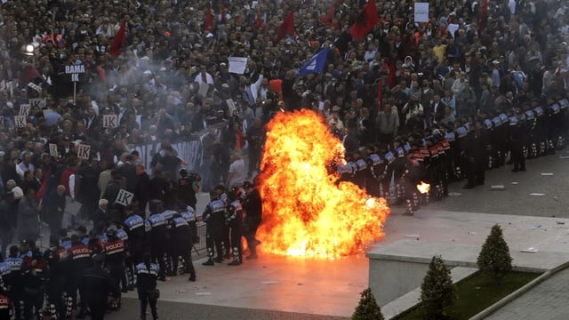 Blick auf zahlreiche Demonstranten. Davor eine Polizeikette und ein Molotow-Cocktail der explodiert und eine Feuerwolke erzeugt. Blick auf zahlreiche Demonstranten. Davor eine Polizeikette und ein Molotow-Cocktail der explodiert und eine Feuerwolke erzeugt.