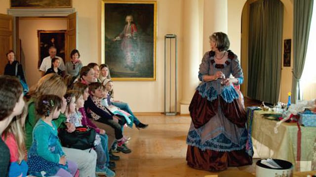 Kostümierte Frau im Museum Schloss Waldegg in Solothurn erklärt vor Kindern etwas. Kostümierte Frau im Museum Schloss Waldegg in Solothurn erklärt vor Kindern etwas.