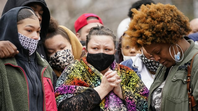 Mehrere Leute mit Masken, die weinen oder zu Boden blicken, umarmen sich und stützen sich aufeinander ab. Mehrere Leute mit Masken, die weinen oder zu Boden blicken, umarmen sich und stützen sich aufeinander ab.