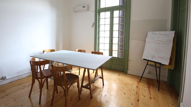 Ein Raum mit Parkettboden, einem kleinen Tisch und einer Flipchart. Ein Raum mit Parkettboden, einem kleinen Tisch und einer Flipchart.