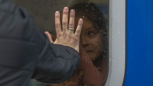 Mädchen im Bus drückt Hand ans Fensterglas, Männerhand drückt von anderer Glasseite zurück.