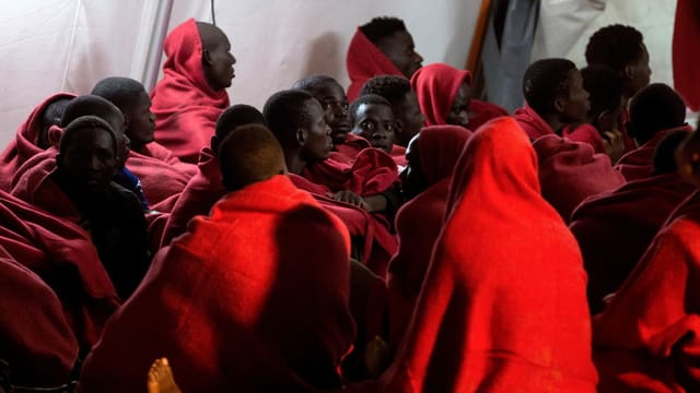 Migranten warten in Decken eingehüllt Migranten warten in Decken eingehüllt